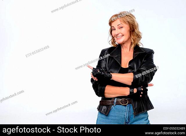 Smiling joyful mature woman in leather jacket pointing at copy space for advertisment or promotional text. Positive emotions, feelings, joy, happiness