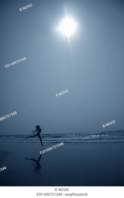 Silhouette of the lady dancing at the beach in deep dark night. Artistic blue colors toning added for coolness of the night