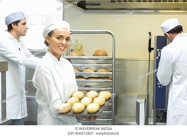 Cute young female baker holding a baking tray with rolls on it
