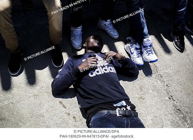 29 June 2018, Spain, Tarifa: An African migrant, originally from the Sub Saharan region, lies down exhausted at the port of Tarifa after being rescued from the...