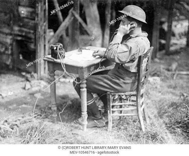 An Allied soldier speaking on a field telephone while sitting at a small table in the open air during the First World War