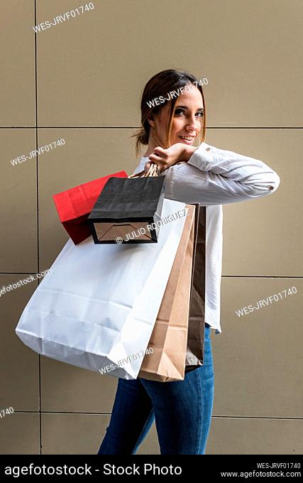 Smiling young woman with shopping bags in front of wall