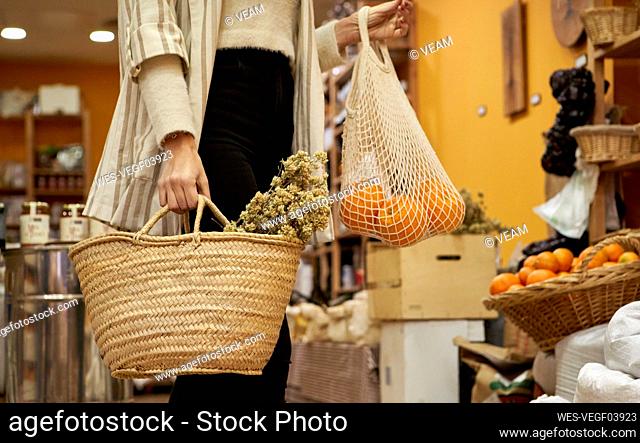 Herbs and Orange fruit in bag held by woman at store