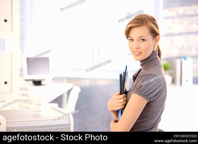 Portrait of attractive secretary, holding file folders. Looking at camera, smiling
