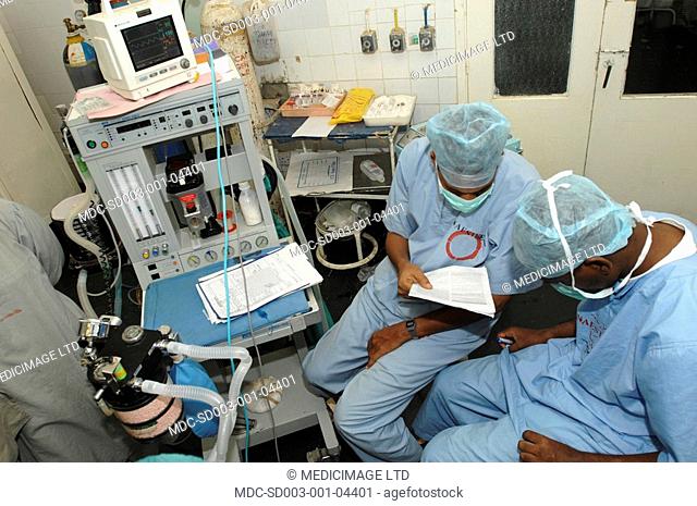 Anaesthetists check patients notes while monitoring the patients vital signs on the anaesthetic machine
