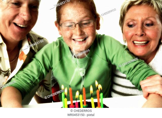 Close-up of a granddaughter looking at a birthday cake with her grandparents and smiling