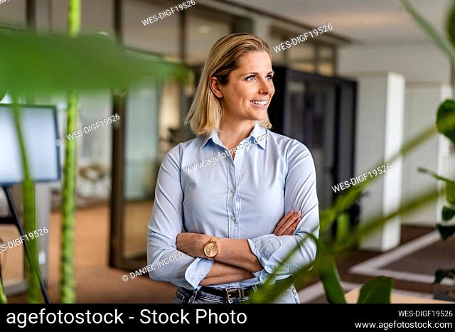 Smiling blond businesswoman with arms crossed in office
