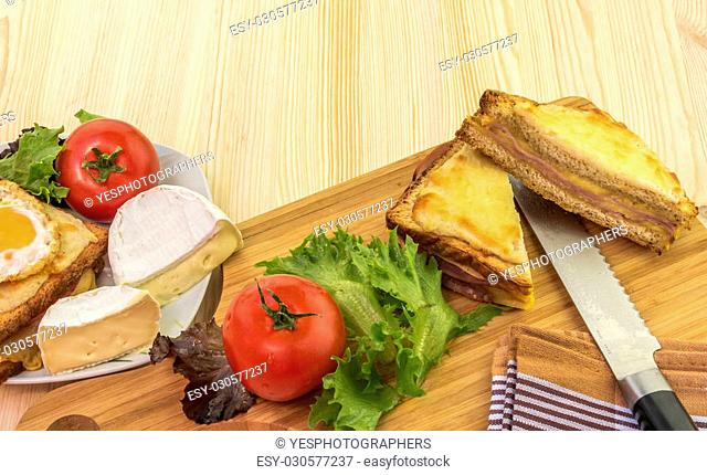 Delicious food on a wooden table, french sandwiches called croque madame and croque monsieur, tomatoes, white cheese and salad
