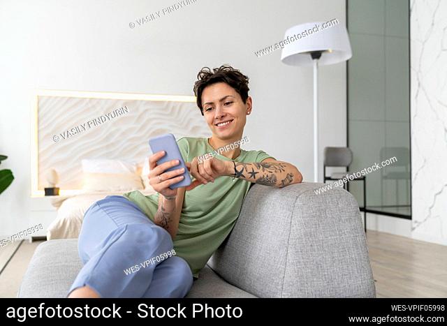 Smiling woman using mobile phone sitting on sofa at home