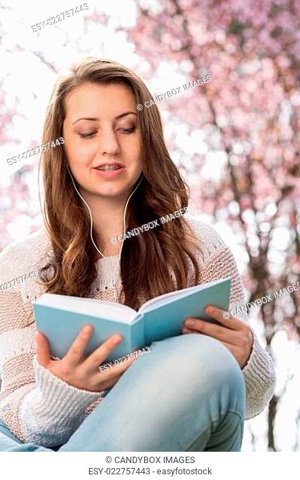 Student reading book near blossoming tree spring