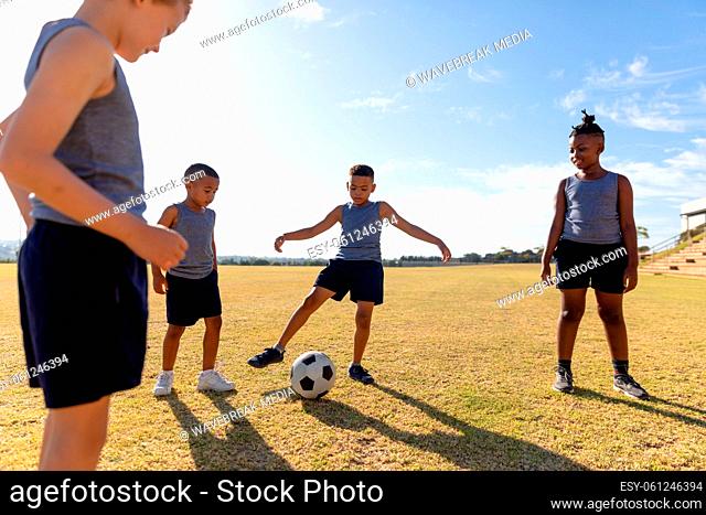 Multiracial elementary schoolboys looking biracial boy kicking soccer ball on field while playing