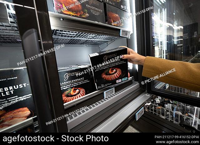 PRODUCTION - 14 December 2021, North Rhine-Westphalia, Mülheim an der Ruhr: A woman takes a pack of shrimp out of the freezer at an Aldi store