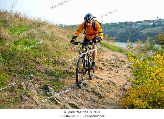 Cyclist in Orange Riding the Mountain Bike on the Autumn Rocky Enduro Trail. Extreme Sport and Enduro Biking Concept