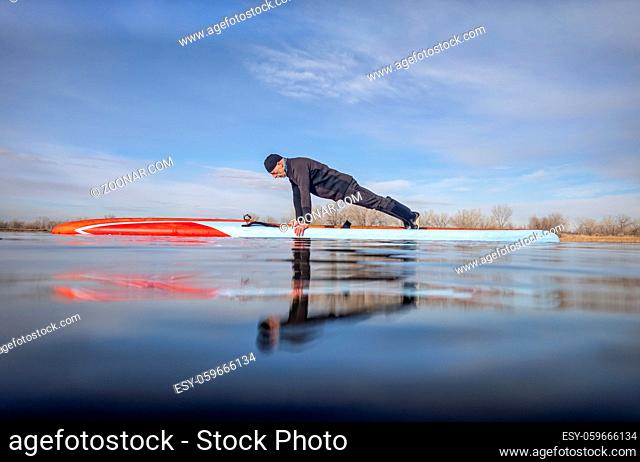 senior male paddler wearing wetsuit is doing push ups on a stand up paddleboard, calm lake in Colorado, early spring, training and fitness concept