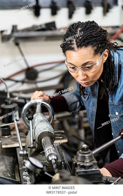 Woman wearing safety glasses standing in a metal workshop, working at a machine