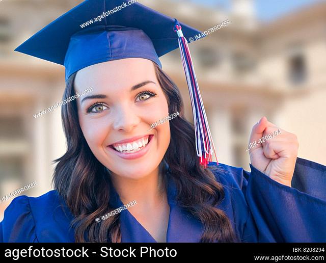 Happy graduating mixed-race woman in cap and gown celebrating on campus