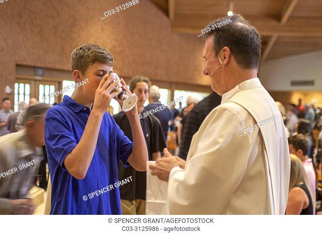 A robed deacon offers the communion cup to a male young adult parishioner at the conclusion of mass at a Catholic Church in Laguna Niguel, CA
