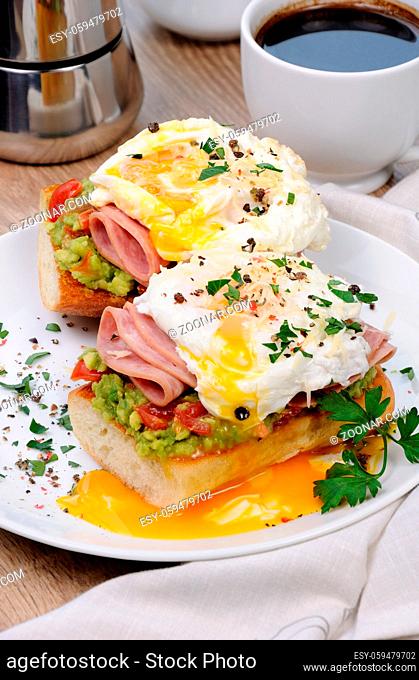 poached eggs with avocado, tomatoes, slices of ham on a baguette for breakfast