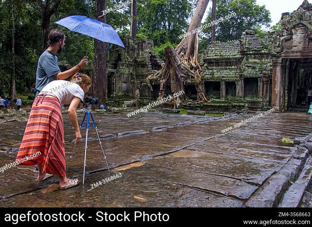 Tourists photographing in the rain at Preah Khan Temple in the Angkor Wat Archeological Park near Siem Reap in Cambodia
