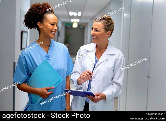 Two diverse female doctors standing in hospital corridor smiling to each other