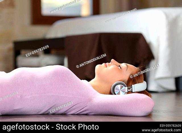 Side view portrait of a woman lying on the floor listening to music with headphones in the bedroom