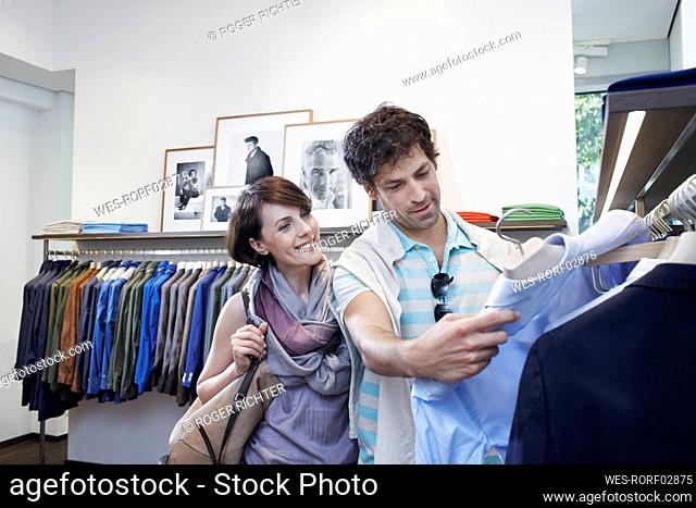 Smiling woman with boyfriend choosing shirt in boutique