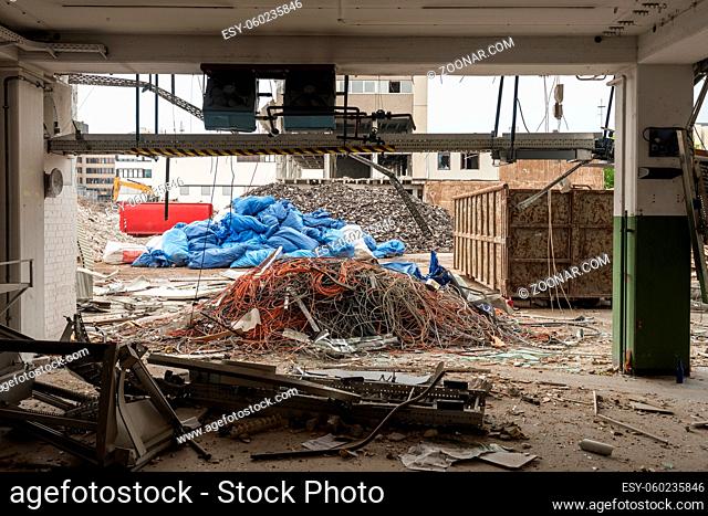 Demolition of large industrial buildings with piles of different parts and heavy machinery as seen through the ground floor of one of the buildings
