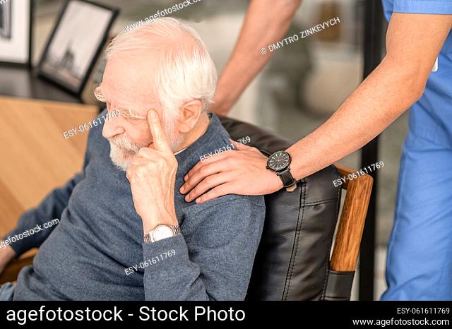 Caring professional medical worker dressed in uniform patting a sad gray-haired man on the shoulder