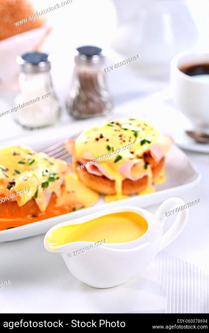 Hollandaise butter sauce in a gravy boat for breakfast served with Eggs Benedict- fried English bun, ham, poached eggs, a cup of coffee