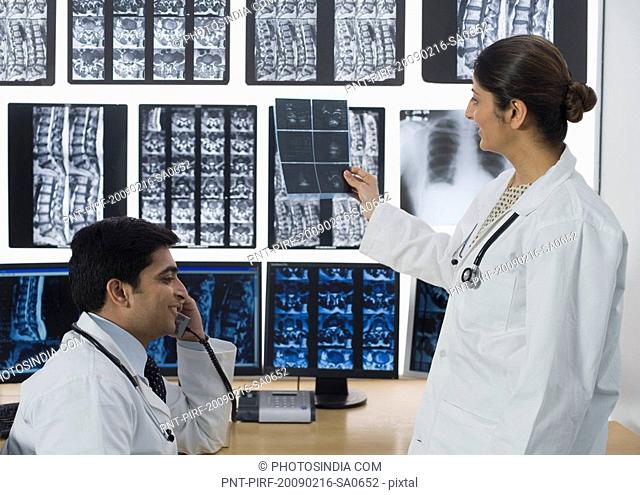 Female doctor examining X-Ray report and her colleague talking on a phone