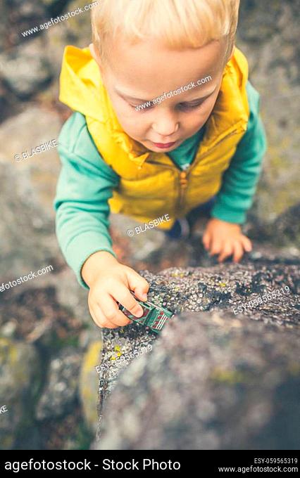 Toddler boy playing with toys on a rock. Little child walking on rocky mountains