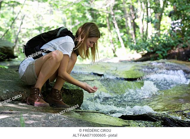 Female hiker drinking water from stream