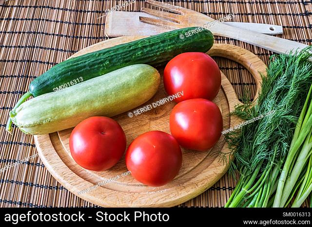 Tomatoes, cucumber, zucchini, greens and a cutting board lie on the kitchen table