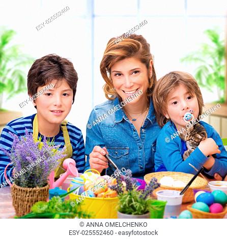 Happy family coloring eggs, mother with two little sons paint traditional Easter eggs in different colors at home, enjoying family tradition