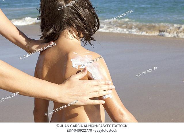 Mother applying sunblock cream to her daughter on arm. Idyllic beach background