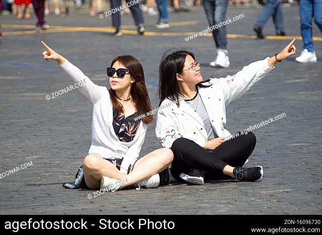 Russia, Moscow, July 29, 2018. Red Square. Young girls are sitting on the asphalt. Tourists point to landmarks
