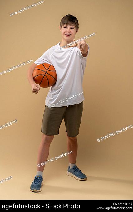 Full-size portrait of a confident teenager with the game ball under his armpit posing against the beige background