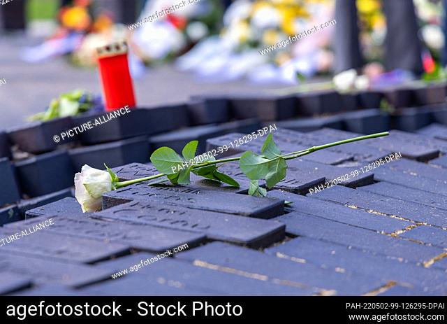 02 May 2022, Mecklenburg-Western Pomerania, Wöbbelin: Flowers and candles stand on a row of stones with names of former prisoners of the concentration camp...