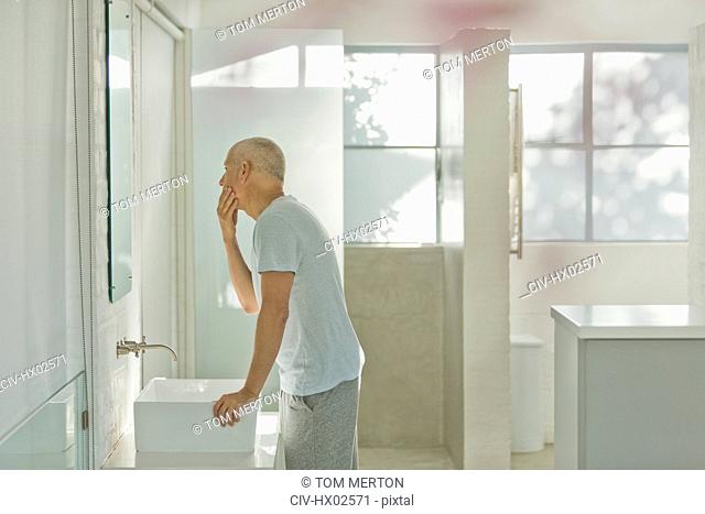 Mature man touching face at bathroom mirror