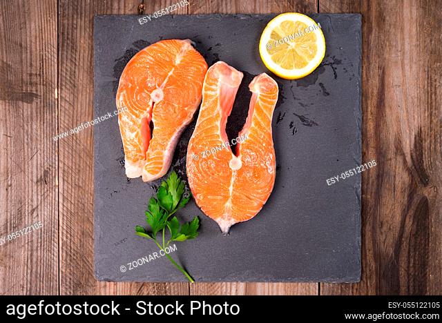 Two fresh raw salmon steaks with lemon and parsley on rustic table