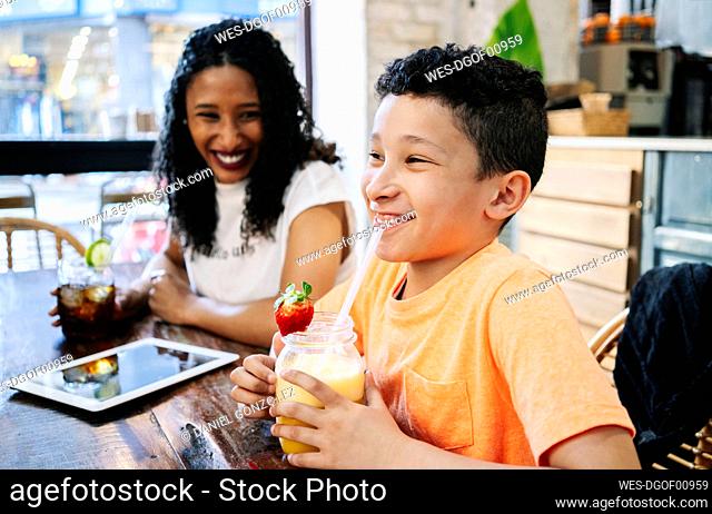 Cheerful woman looking at son sitting with fresh smoothie in restaurant