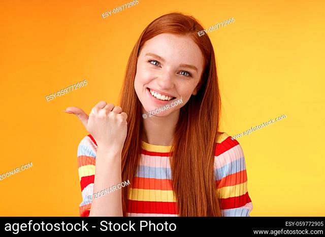 Friendly tender feminine kind redhead woman blue eyes pointing thumb left showing location where find product copy space gladly help discuss interesting promo...