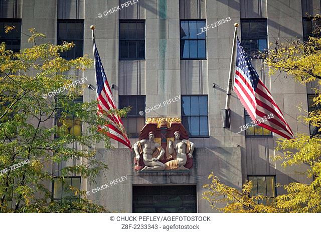 USA flags and sculpture of Adam and Eve on building facade at Rockefeller Center in Midtown Manhattan, New York, NY