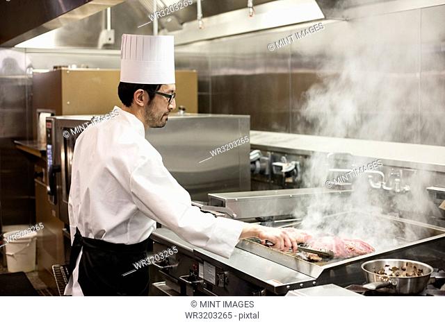 An Asian chef working with fresh meat on the grill in a commercial kitchen