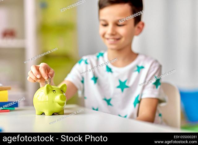 little boy putting coin into piggy bank at home