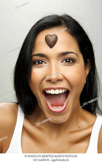 Latin girl looking surprised at the camera with a valentine's chocolate heart on her forehead