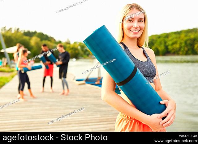 Lächelnde junge Frau mit Yogamatte nach einem Fitness oder Yoga Kurs in der Natur