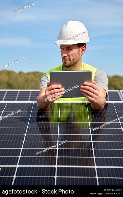 Engineer wearing hardhat using tablet PC between solar panels on rooftop