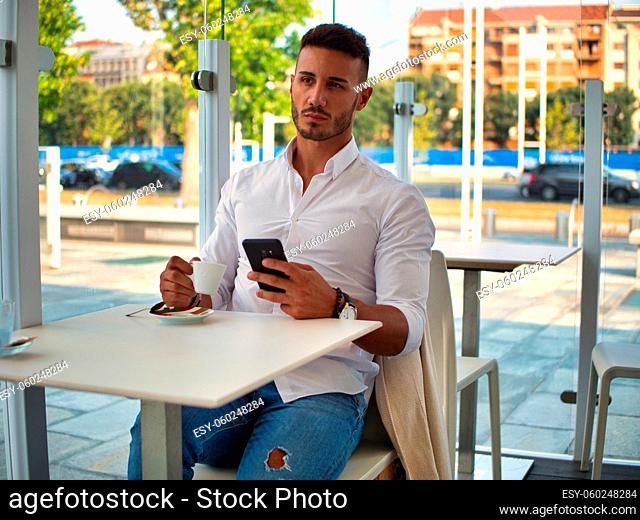 Close up of Handsome Young Man Drinking Coffee at the Shop While Looking at Cell Phone