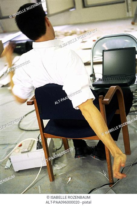 Man sitting in chair stretching arms, in front of laptop computer on chair
